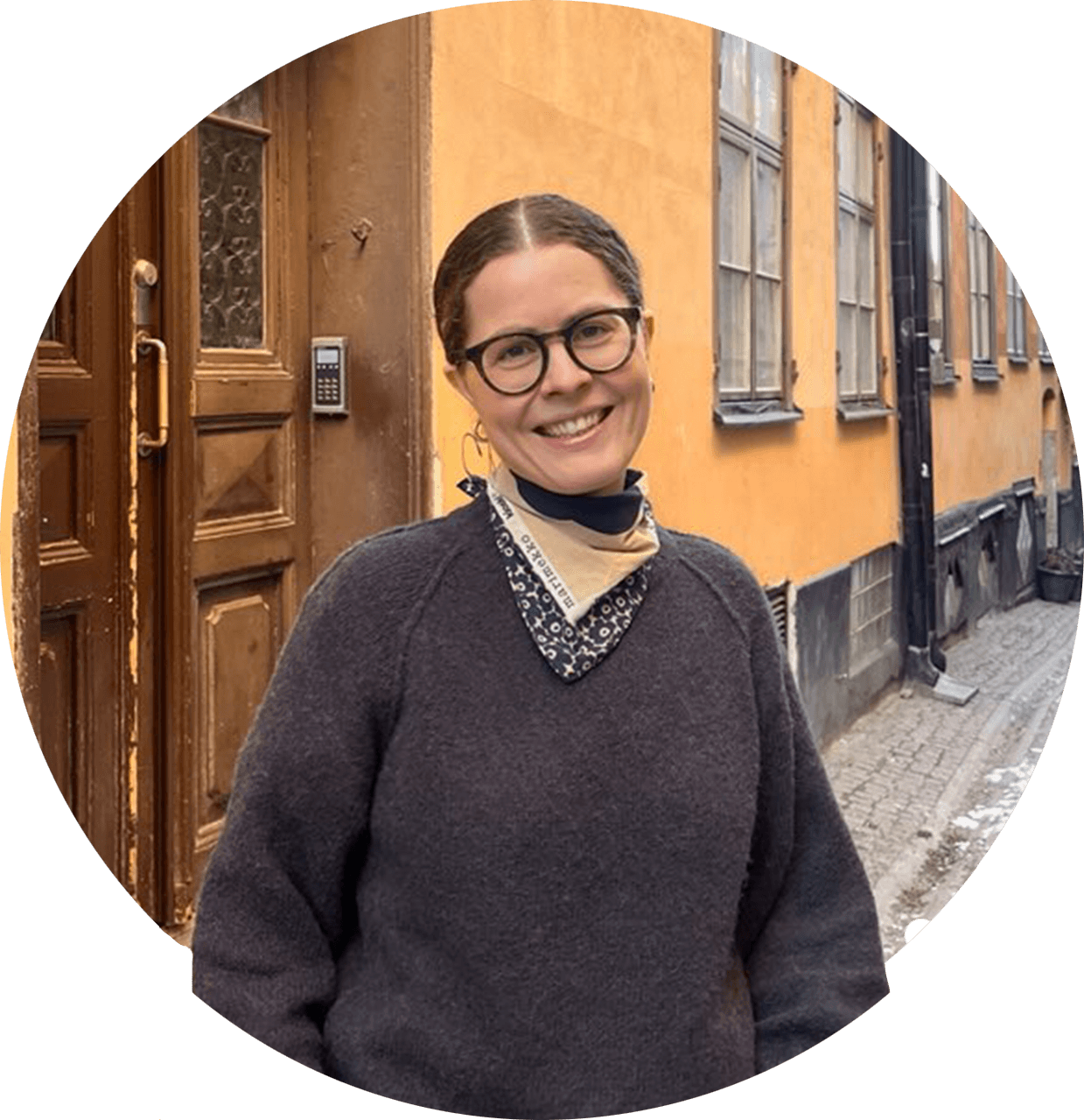 Ingunn, en smilende kvinne med oppsatt brunt hår og mørke briller. Hun har en grå strikkegenser og et mønstret skjerf.