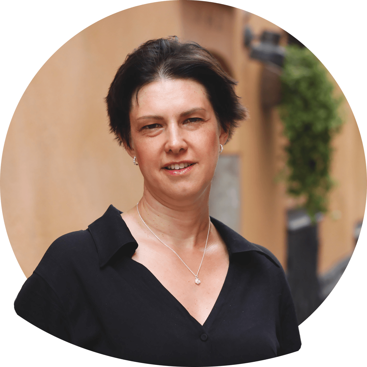 Sandra smiler i rødbrun kort frisyre i hvit v-utringet topp. Foto.