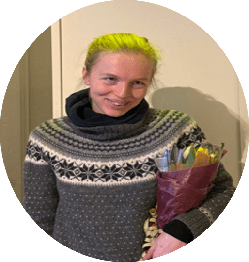 Amalie med lyst hår, iført grå mønstret genser, som holder en bukett blomster.